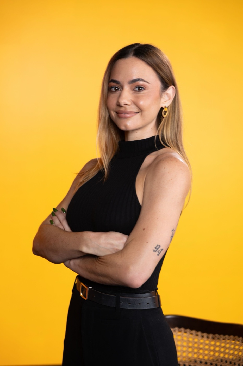 Kelly standing with arms crossed against a yellow backdrop